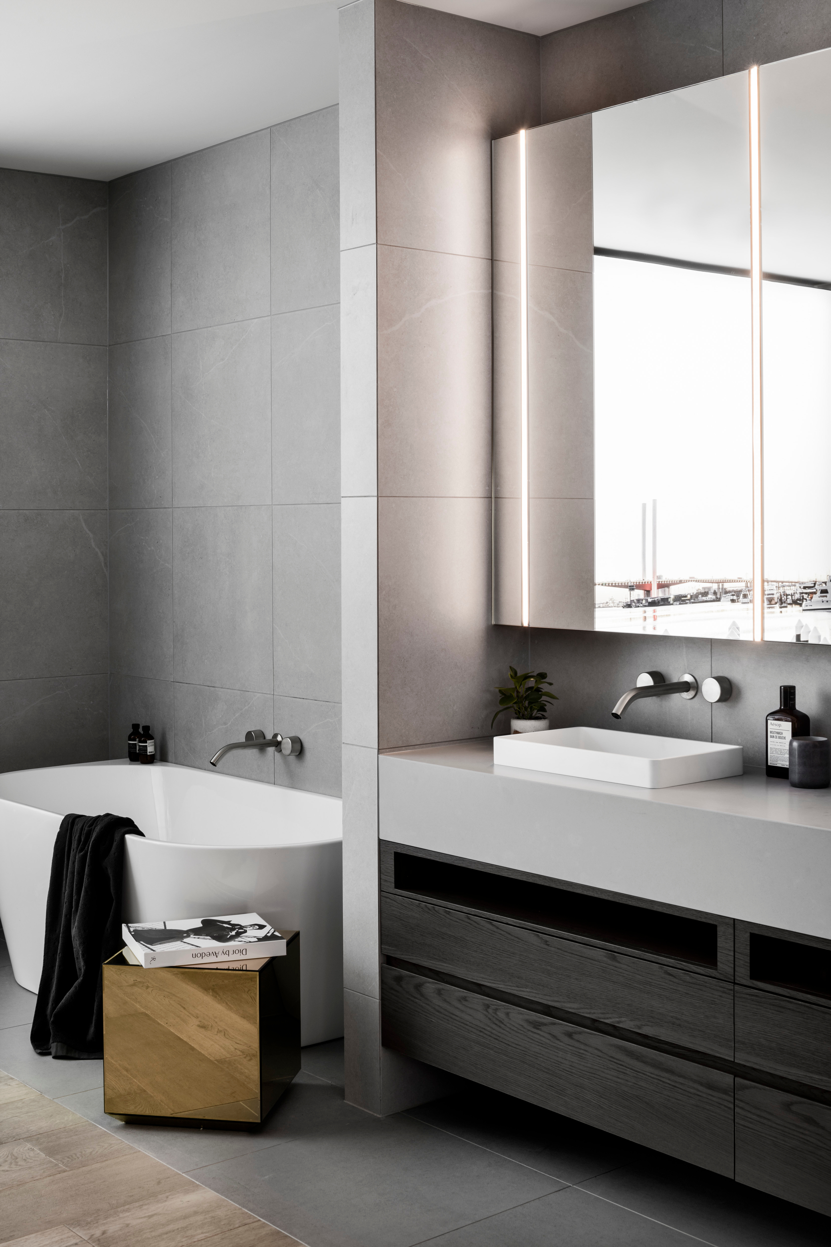 A contemporary bathroom featuring a bath, a generous mirror and custom joinery crafted from Cellupal stunningly accurate timber-look laminate in Sparka, a grey decor with 3D woodgrain feature and a super matt finish.