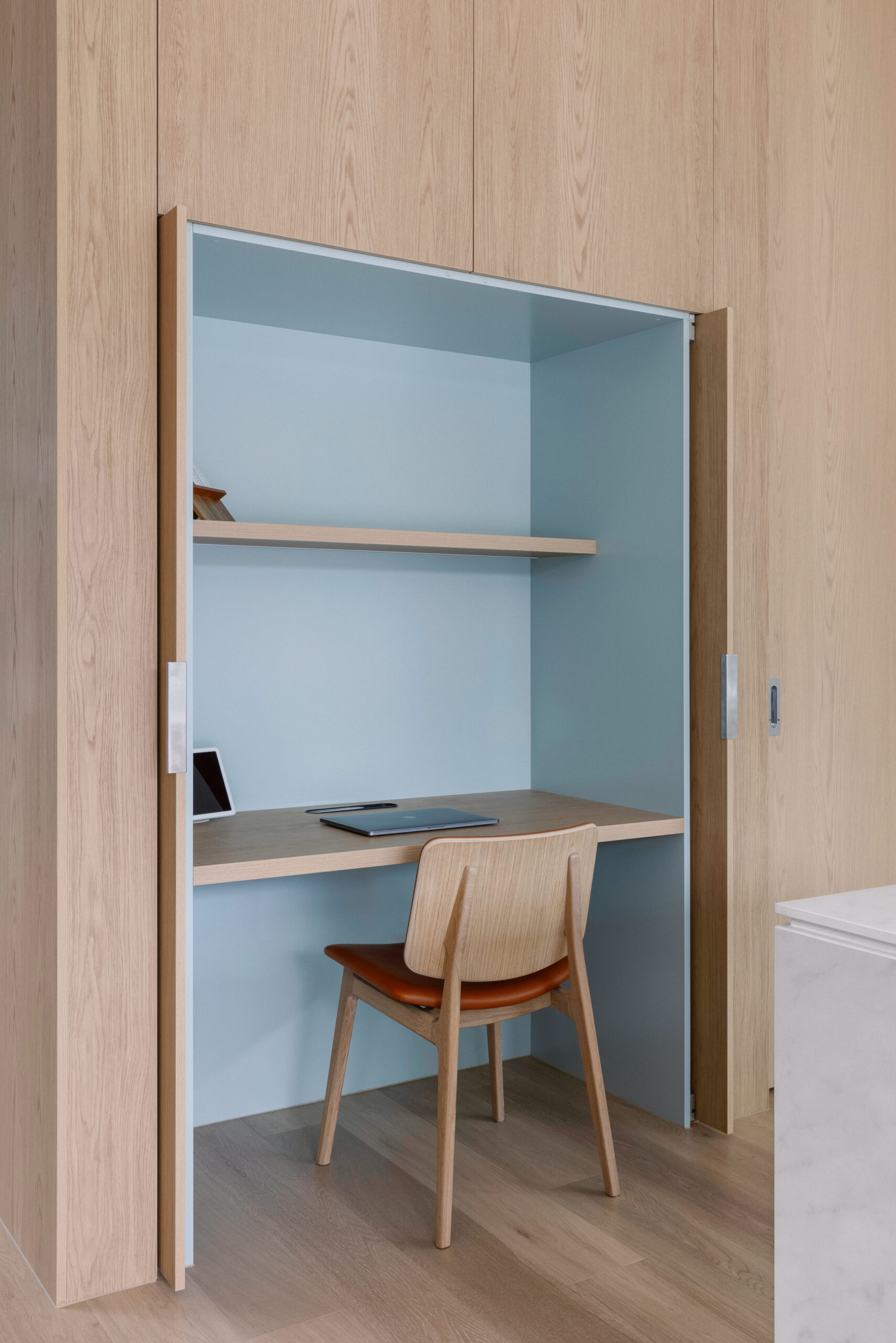 A compact workspace nook with a minimalist design, striking pale blue accent walls and oak effect laminate joinery, crafted from Cellupal Eik, a stunningly accurate timber-look laminate from George Fethers and Co.