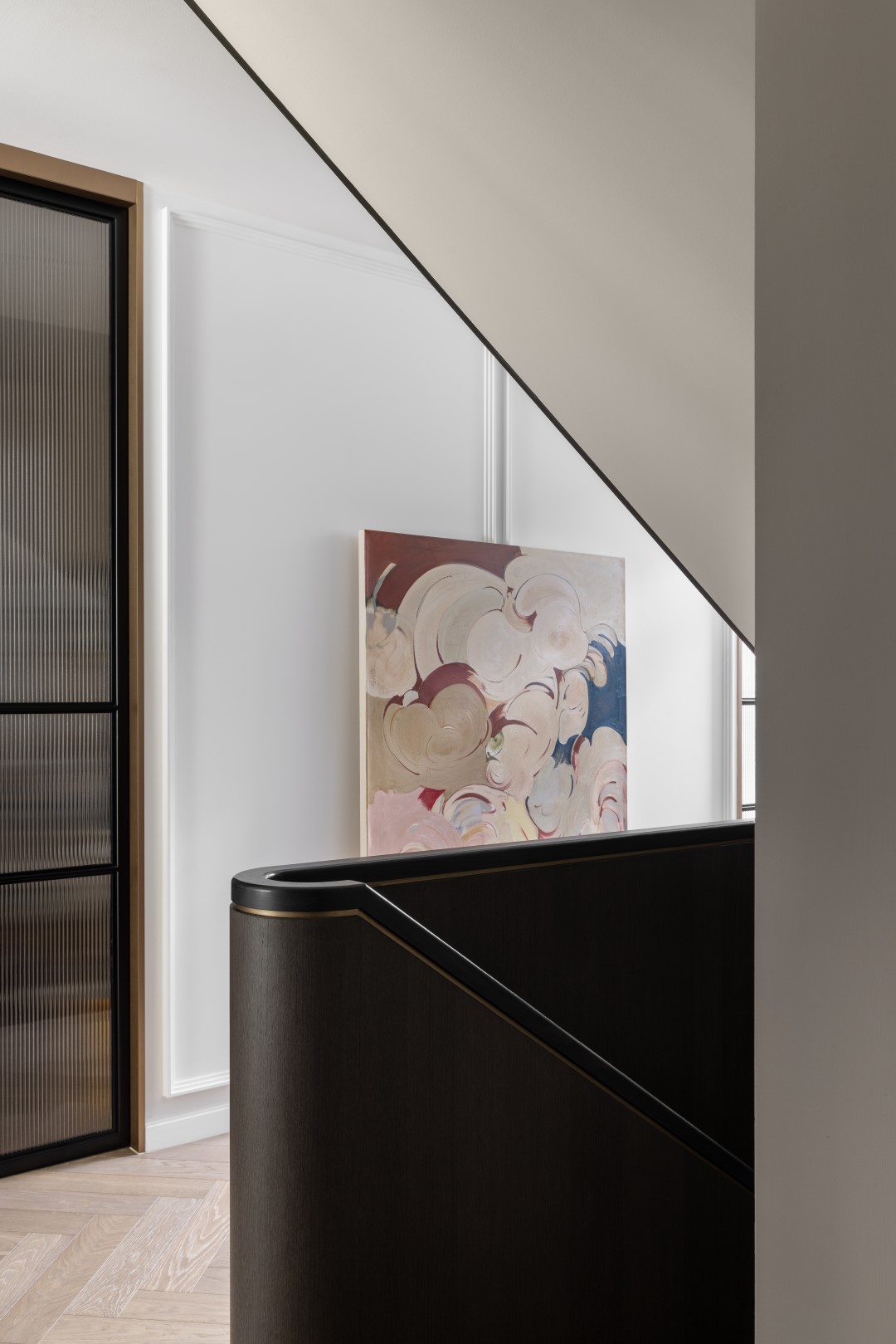 A close-up view of an elegant custom staircase featuring Lignapal prefinished timber veneer in 151.07 Cinder Gum. The staircase's sleek, curved design is highlighted by the dark timber veneer, contrasted against a bright, minimalist interior space adorned with contemporary artwork.