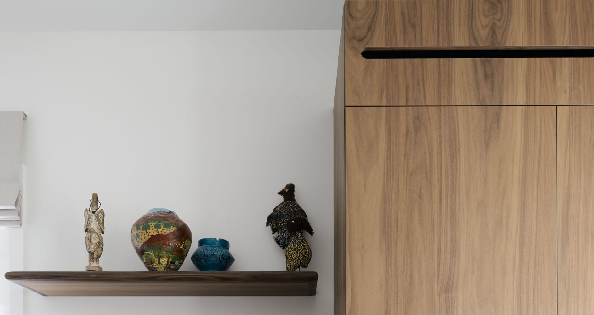 A close-up of custom cabinetry at Finch House, crafted from Lignapal walnut veneer sheets. The warm timber with featured crown cut wood grain pairs beautifully with a vibrant collection of sculptural art displayed on a floating shelf.