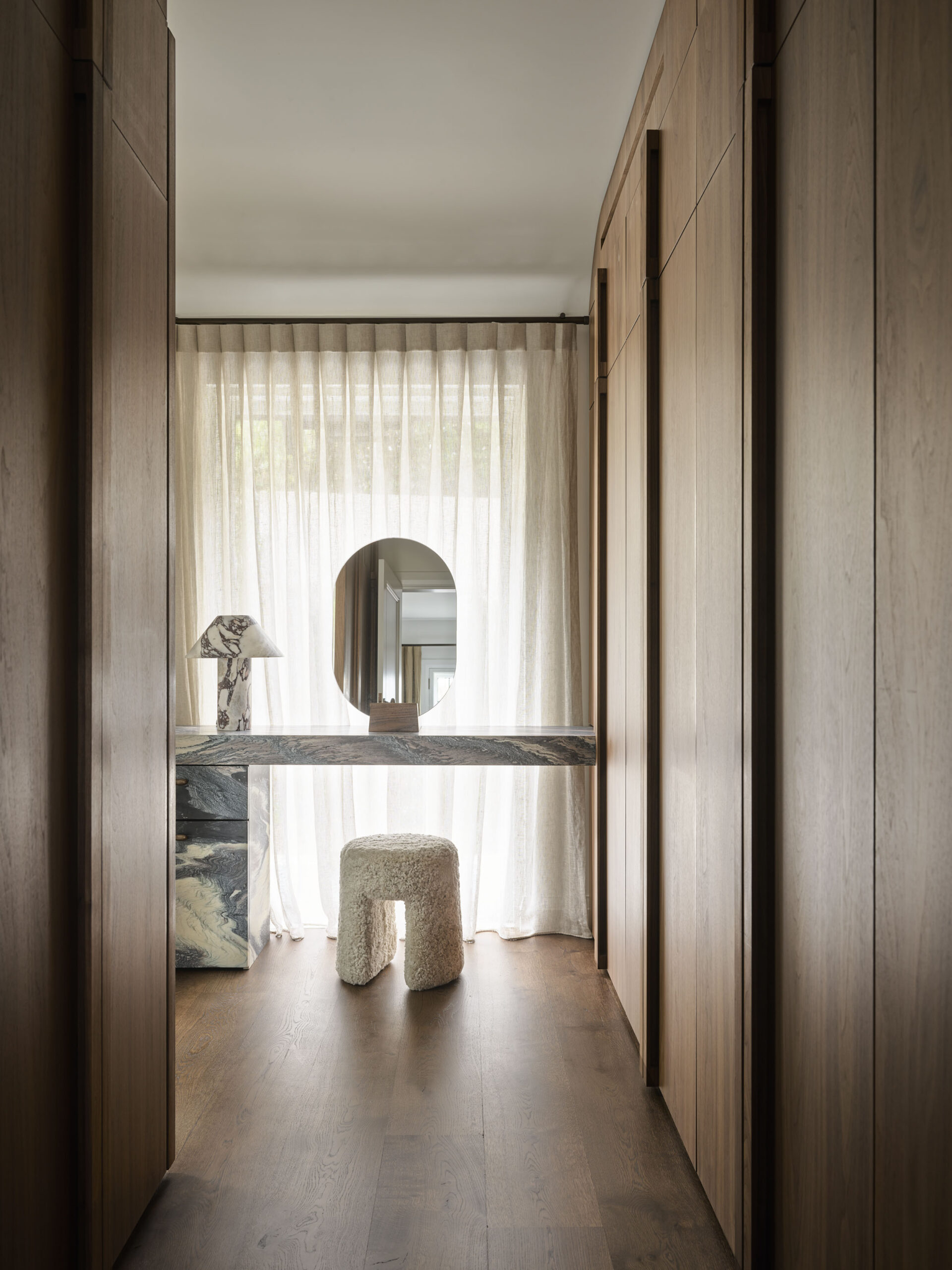A beautifully designed dressing area at Finch House, featuring floor-to-ceiling joinery crafted from Lignapal walnut veneer panels. Natural light filters through soft curtains, highlighting the warm tones of the timber and a striking marble vanity